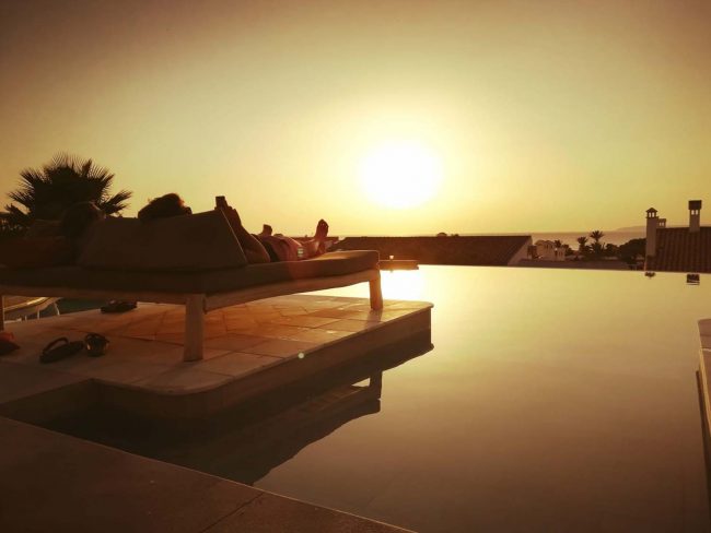 personas tumbadas en hamacas viendo el atardecer en la piscina infinity del hotel el cortijo de zahara